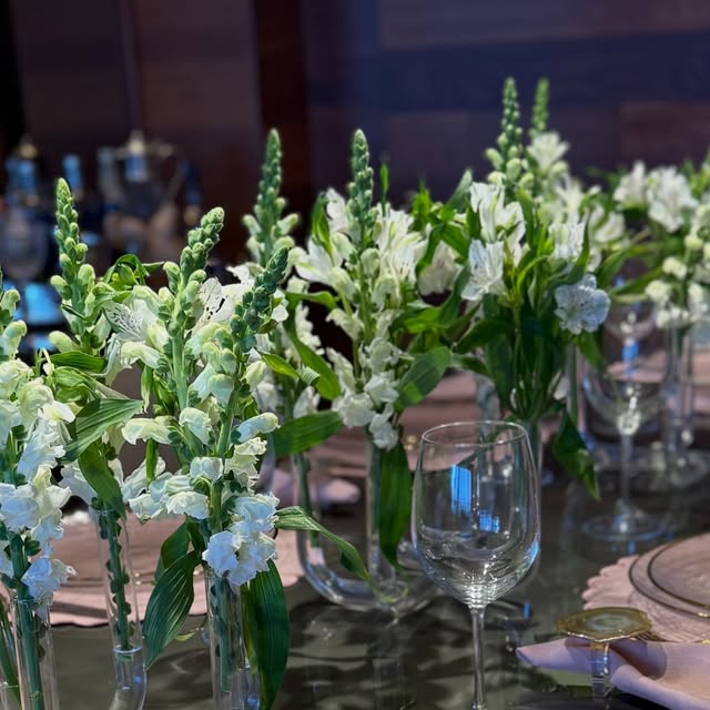 Mesa de jantar longa com arranjos de flores brancas e taças