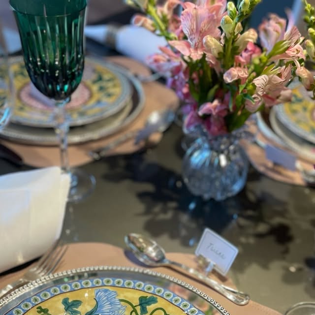 Mesa posta com pratos florais, taças e arranjo de flores rosa