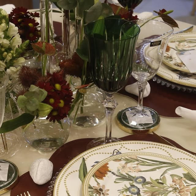 Mesa posta com prato floral, taças de cristal e arranjo de flores