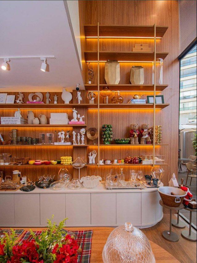 Interior da loja TD Home: estante de madeira iluminada com vasos, esculturas e cristais