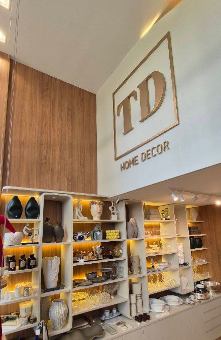 Parede da loja TD Home Decor com o logo em relevo, sobre as estantes de peças